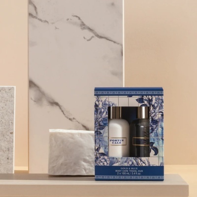 Conjunto cuidados corporais Gold & Blue em embalagem azul com padrão floral contendo dois frascos de 100 ml, um branco e um preto com tampa prata.