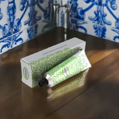 Tubo de creme verde e branco com embalagem sobre superfície metálica, fundo de azulejos azuis e brancos