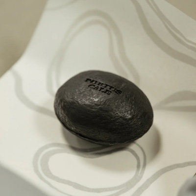 Sabonete preto oval com texto PORTUS CALE na superfície branca com padrões cinzentos