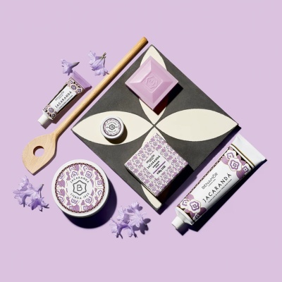 Produtos de cosmética Jacaranda da Benamôr com embalagens florais e sabonete lilás, colher de madeira e flores lilás