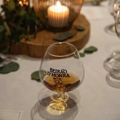 Taça com bebida castanha e texto BEIRÃO DHONRA numa mesa branca