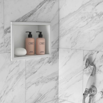 Prateleira branca com duas garrafas rosa e um sabonete branco numa parede de mármore