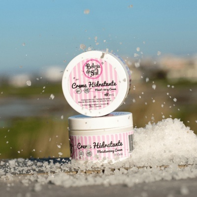 Dois frascos de creme hidratante com embalagem branca e rosa sobre sal grosso