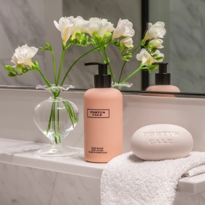 Sabonete branco, loção pêssego e flores brancas num vaso em bancada de mármore com toalha branca