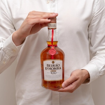 Frasco de licor Beirão dHonra com tampa e selo em destaque, segurado por uma pessoa com camisa branca.