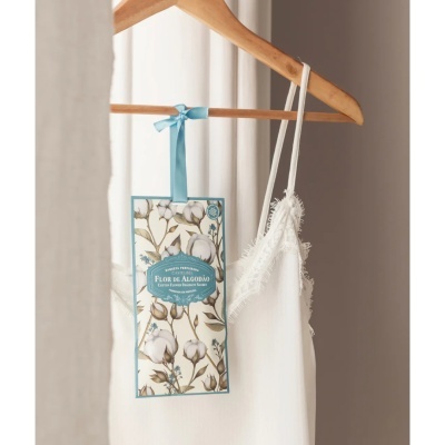 Sachet perfumado Castelbel Flor de Algodão pendurado num cabide de madeira ao lado de vestido branco delicado