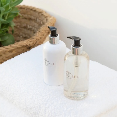 Dois frascos com dispensador branco e transparente sobre toalha branca com cesto de fibras e planta