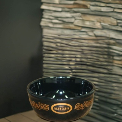 Taça preta decorativa em cerâmica com texto vintage e parede de pedra ao fundo.