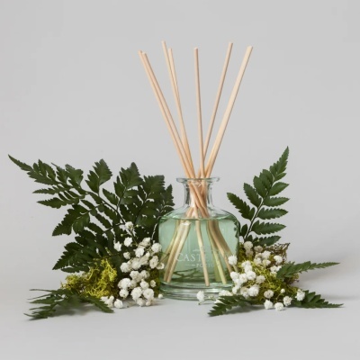 Difusor de aroma em vidro com varetas de madeira e decoração de folhagens e flores brancas