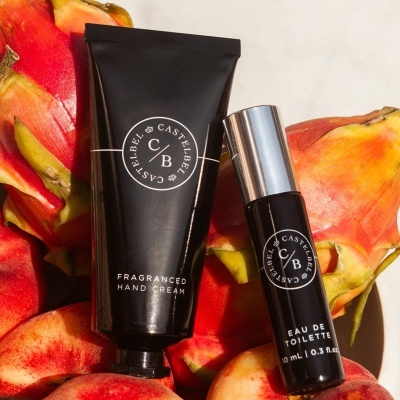 Duas embalagens Castelbél C/B preta, creme para mãos e eau de toilette, com frutos vermelhos ao fundo.