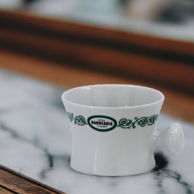 Copo branco de cerâmica decorado com texto verde e arabescos, em mesa de mármore