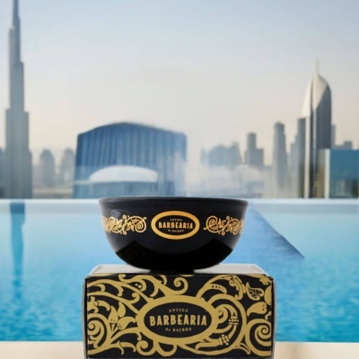 Taça preta decorada com padrão dourado e texto ANTIGA BARBEARIA de BAIRRO com caixa e vista de piscina e cidade ao fundo