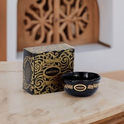 Taça preta de barbear com detalhes dourados ao lado de uma caixa decorativa preta com detalhes dourados