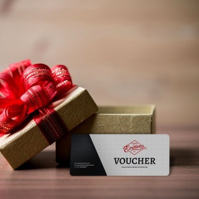 Caixa de presente dourada com fita vermelha e voucher branco e preto sobre mesa de madeira