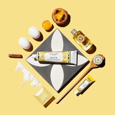 Produtos Benamôr com creme NATA, óleo, ovos, pastel de nata e utensílios sobre fundo amarelo.