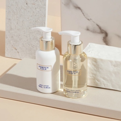 Dois frascos cosméticos com tampas brancas e detalhes dourados numa superfície neutra