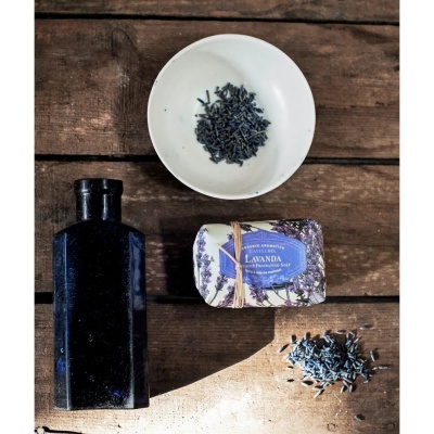 Frasco azul, sabonete Lavanda Castelbel, prato branco com lavanda sobre madeira.