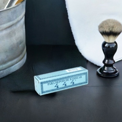 Pincel de barbear, caixa para pós-barbear e balde metálico sobre superfície preta