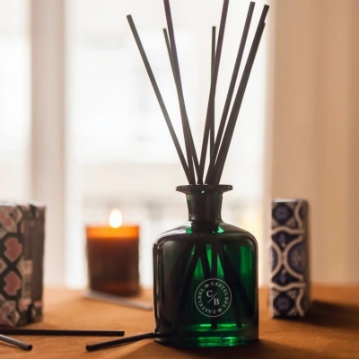 Frasco verde com difusor de varetas em mesa com vela e caixas decorativas