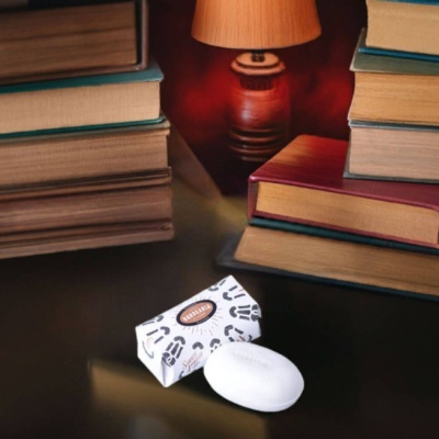 Barra de sabão branca com embalagem com padrão preto junto a livros e lâmpada