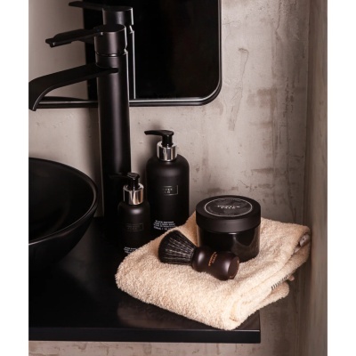 Produtos de cuidados pessoais pretos em bancada de casa de banho com toalha bege e escova de barbear