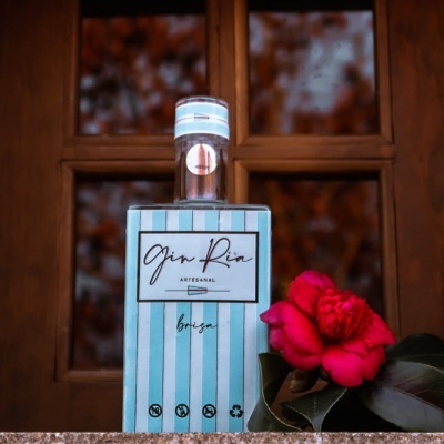Garrafa de gin artesanal azul e branca com flor vermelha ao lado