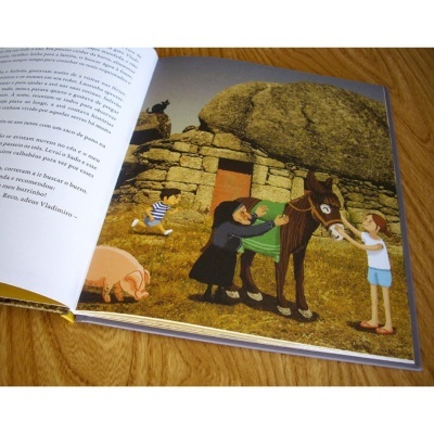 Livro infantil aberto com ilustração de casa de pedra, burro verde e personagens animados.