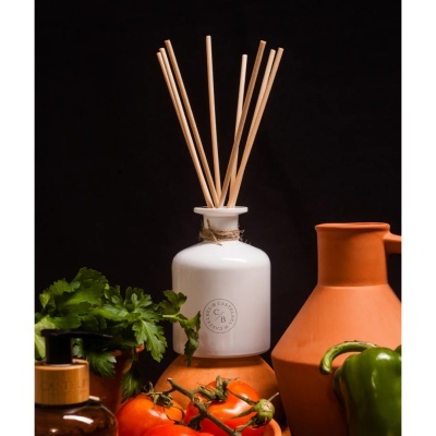 Frasco branco de cerâmica com pauzinhos de difusor e legumes frescos