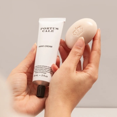 Creme de mãos em tubo branco e sabonete oval bege com brasão nas mãos.