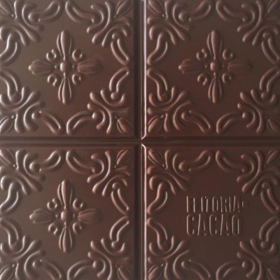 Tablete de chocolate castanho com padrão decorativo em relevo e texto HISTÓRIA CACAO