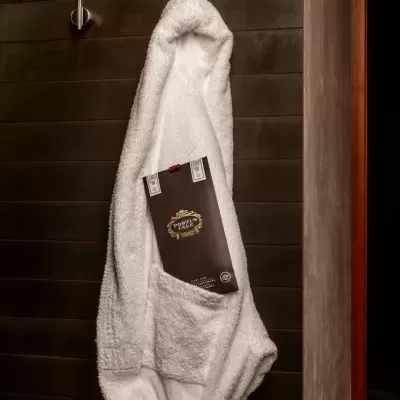 Robe de banho branco pendurado numa parede escura com etiqueta PORTUS CALE