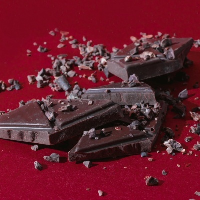 Chocolate preto partido com pedaços de cacau numa superfície vermelha