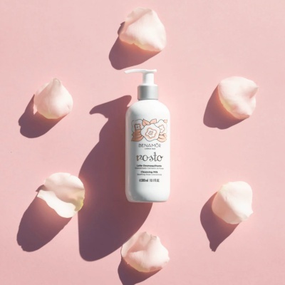 Frasco branco de leite desmaquilhante Benamôr com pétalas de rosa sobre fundo rosa.