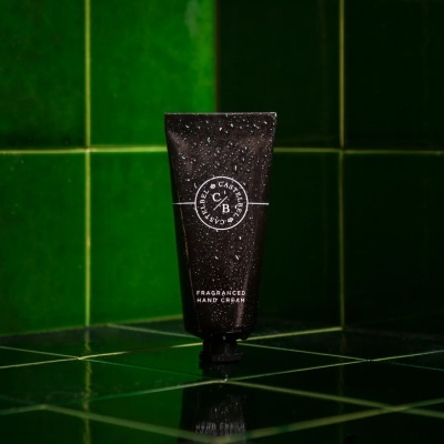 Tubo preto de creme para as mãos molhado sobre azulejos verdes.