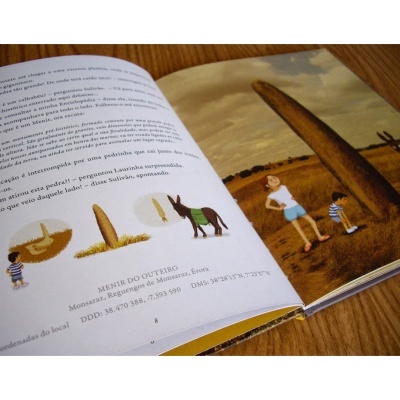 Livro infantil aberto com texto, ilustrações de crianças e burro, e foto de menir na paisagem.