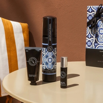 Conjunto de creme de mãos, sabonete e perfume em embalagens pretas com detalhes azuis e brancos sobre mesa redonda bege