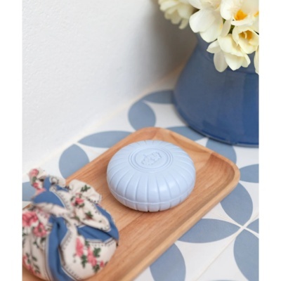 Sabonete redondo azul claro na bandeja de madeira com saco floral e vaso azul em azulejos azuis e brancos.