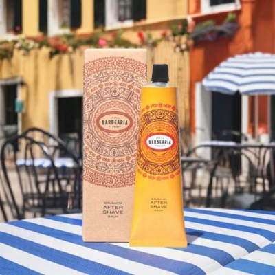 Creme bálsamo after shave amarelo com embalagem de cartão e padrão circular, em mesa exterior às riscas azul e branca.