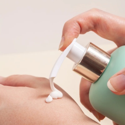 Frasco verde com dispensador a aplicar creme branco na mão