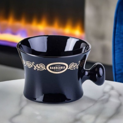 Copo preto com decoração dourada e texto em relevo numa superfície branca