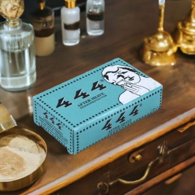 Caixa azul de after shave 444 sobre móvel em madeira com frascos e objetos dourados