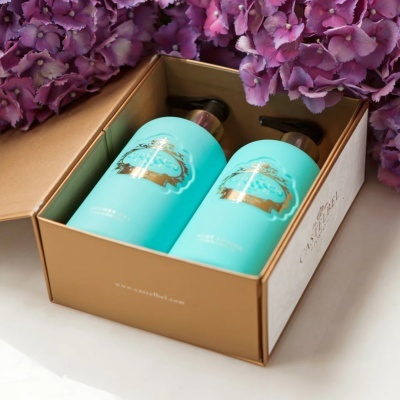 Conjunto de dois frascos de plástico azul turquesa numa caixa castanha com tampa aberta e flores lilases ao redor.