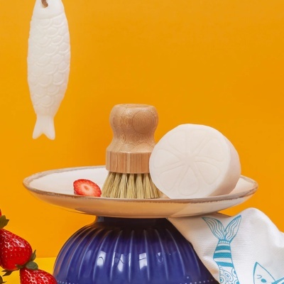 Escova de cozinha, sabonete e morangos sobre prato branco com base azul, fundo amarelo