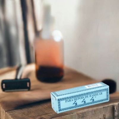 Caixa azul clara com texto para depois de barbear sobre superfície de madeira com lâmina de barbear e frasco desfocado ao fundo