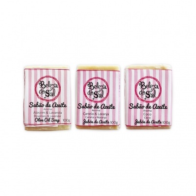 Três sabonetes de azeite embalados com rótulos rosa e branco com textos diferentes
