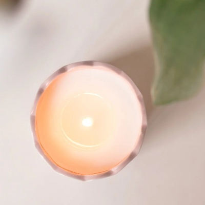 Vela acesa branca em recipiente cerâmico rosa claro com bordas facetadas