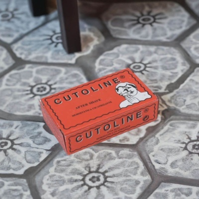 Embalagem vermelha de after shave Cutoline sobre azulejos hexagonais com padrão cinza