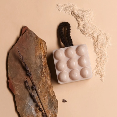 Sabonete branco com bolhas e alça preta junto a pedra e flores secas sobre fundo bege.