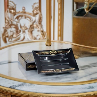 Cinzeiro negro com detalhes dourados sobre mesa de mármore com moldura dourada