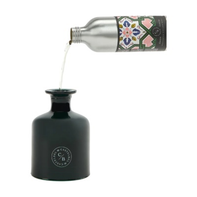 Garrafa metálica prateada a verter líquido em recipiente cerâmico verde escuro com logotipo CASTELBEL C/B.